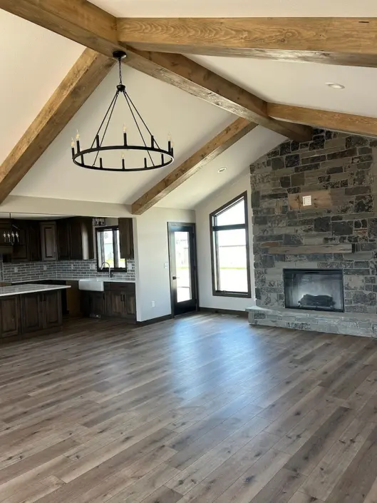 Open-concept living room with stone fireplace and wood beams in a Redi-Built home
